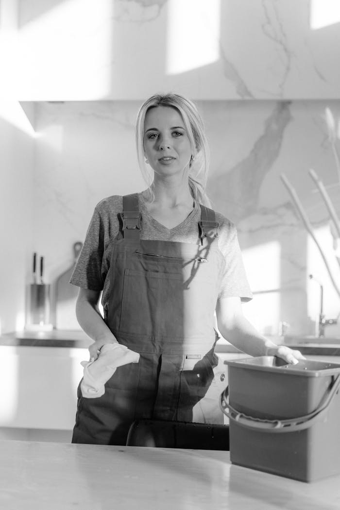 Black and white portrait of a housekeeper with cleaning supplies in a modern kitchen.